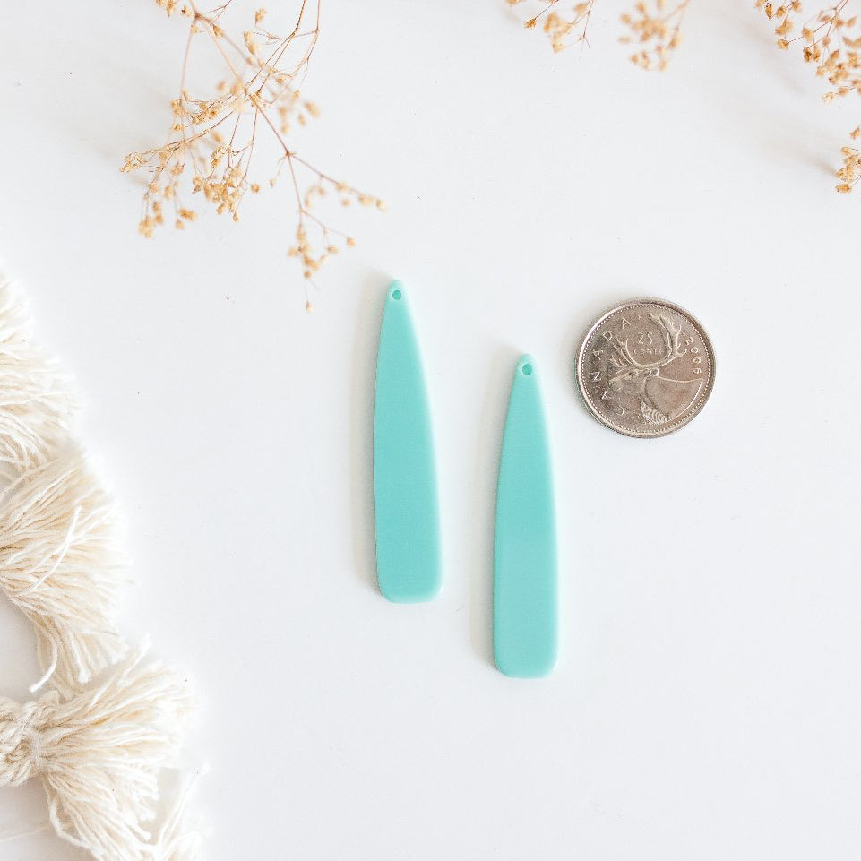 Two turquoise earrings on a white surface with a coin for scale and decorative elements.