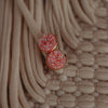 "Pink sparkly faux druzy earrings set in rose gold, resting on a textured woven basket surface, casting graceful shadows.