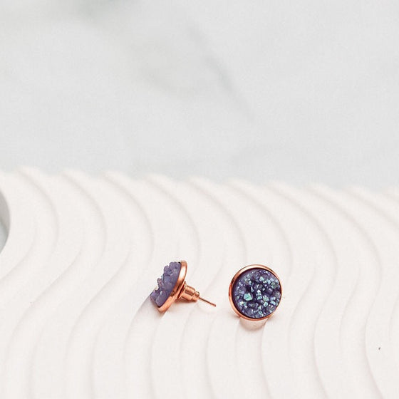 "Shimmering lavender rose gold stud earrings elegantly displayed on a white wavy plate background, capturing the play of light and color. The sparkling gems exude charm and sophistication, creating a captivating visual contrast against the serene backdrop.