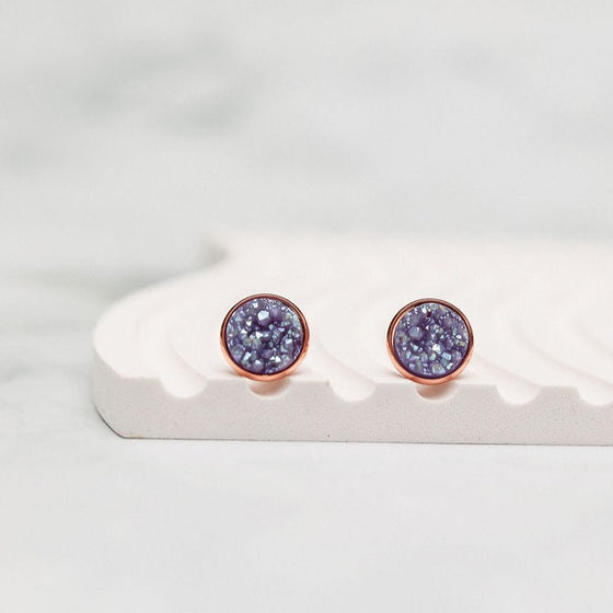 Shimmering lavender rose gold stud earrings elegantly displayed on a white wavy plate background, capturing the play of light and color. The sparkling gems exude charm and sophistication, creating a captivating visual contrast against the serene backdrop.