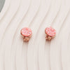 "Two pink sparkly faux druzy earrings set in rose gold clip-on style. One showcases the front with shimmering pink faux druzy gems, while the other displays the back clip-on mechanism. Both earrings elegantly laid on an off-white wavy plate background."